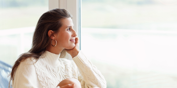 Woman in sweater gazing out of the window in thoughtful pose. A New Hope Counseling Center, Lansing MI